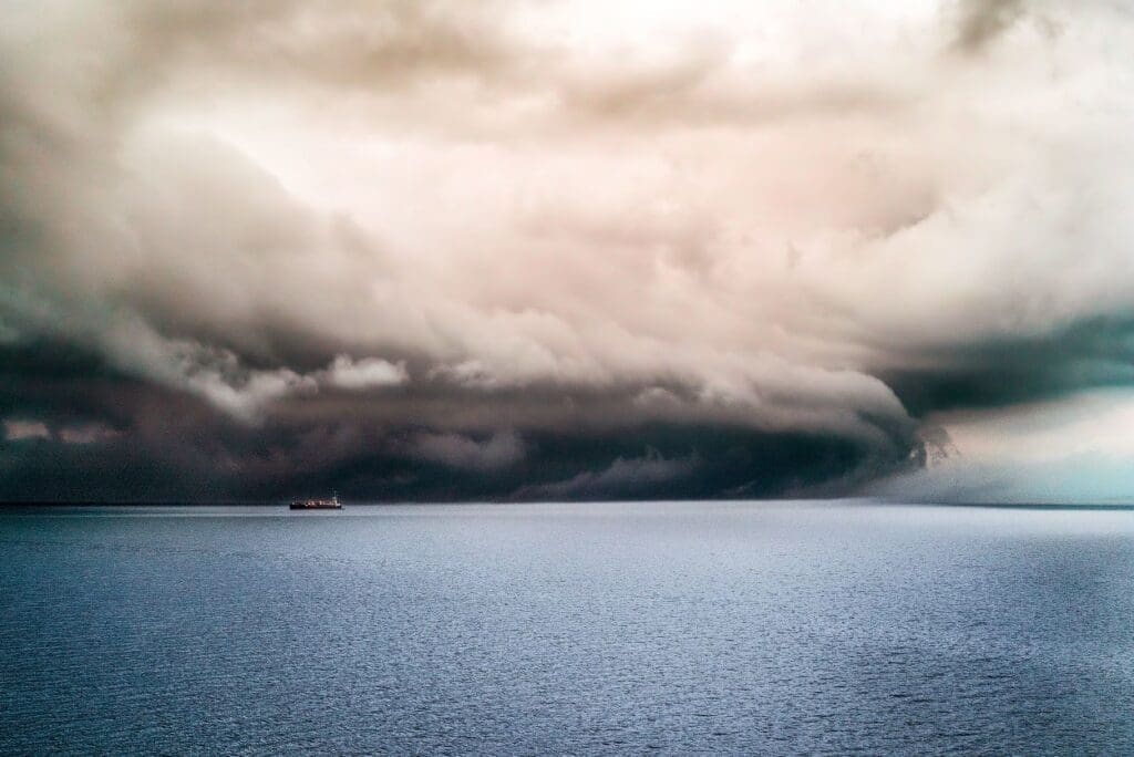 Image: Big dark clouds covering the pure ocean with a ship sailing in it