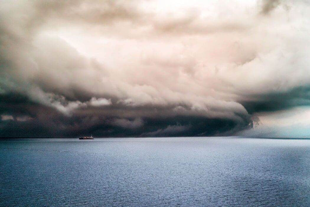 Image: Big dark clouds covering the pure ocean with a ship sailing in it
