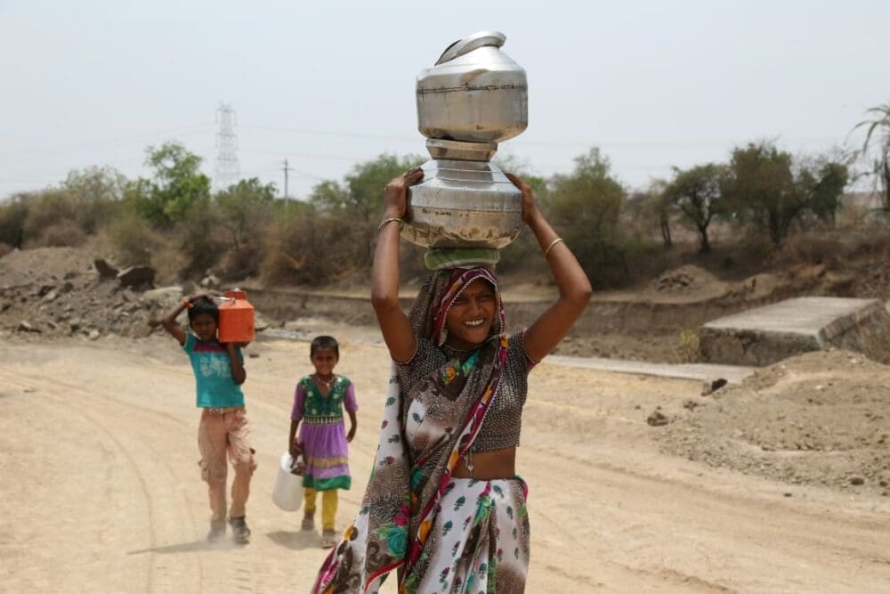 Image: woman in green and white dress holding white ceramic jar