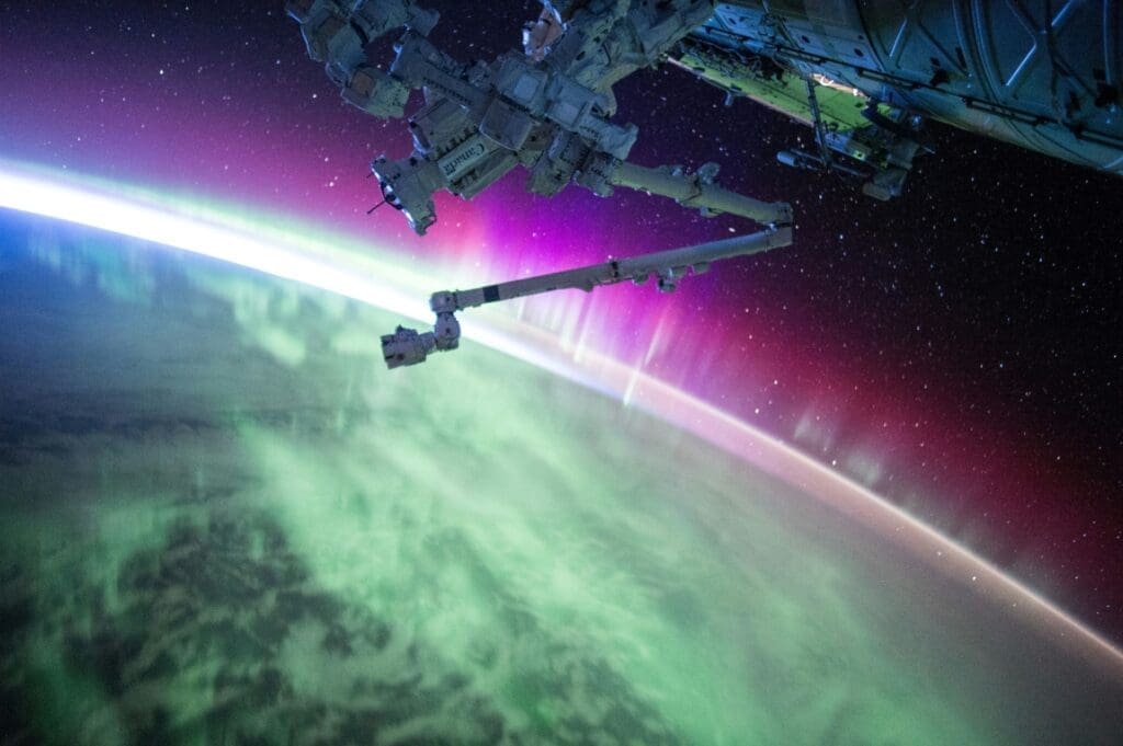 Image: Photography of purple and green aurora beam below grey space satellite