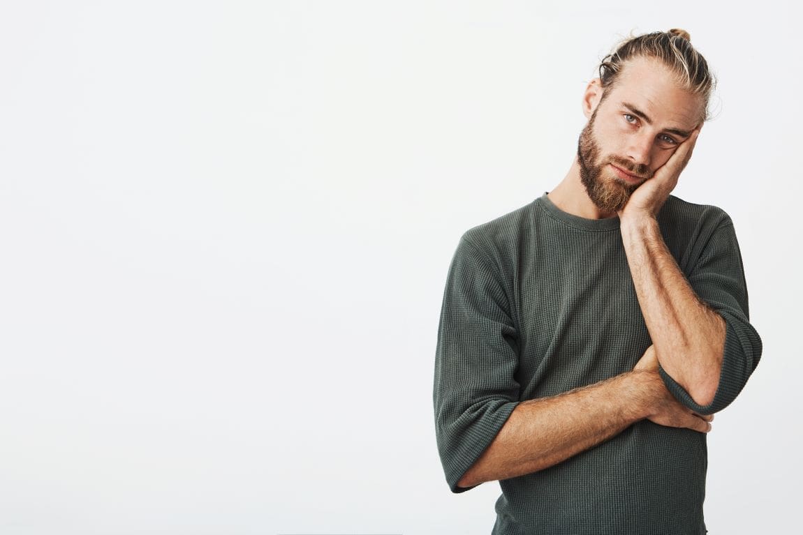 Image: Portrait of unhappy mature bearded guy in grey shirt holding hand on cheek exhausted and tired (s. eco-guilt, eco-shame)
