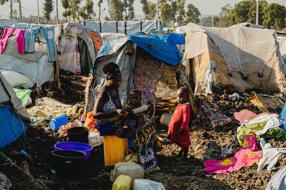 Image: Mother with Kids Sitting Among Tents in Camp (s. aid cuts)