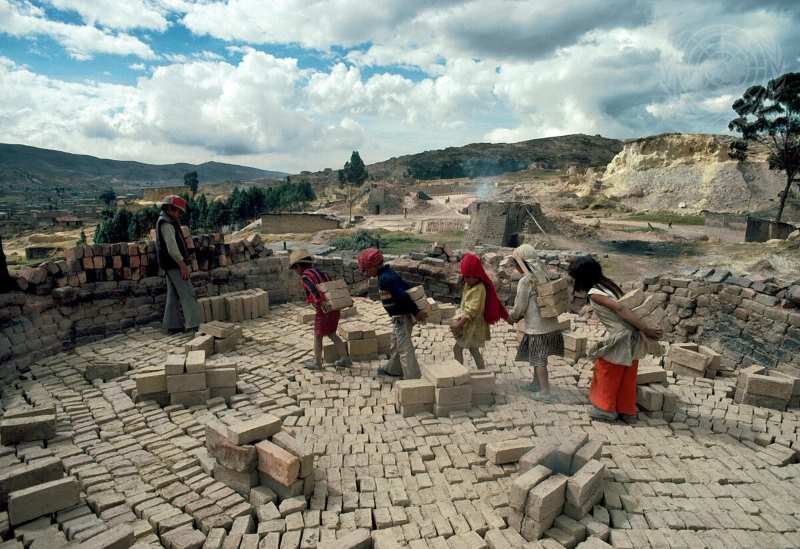 Image: Children at a brick factory act as human wheelbarrows, hauling bricks from place to place on their backs (s. modern slavery, forced labor)