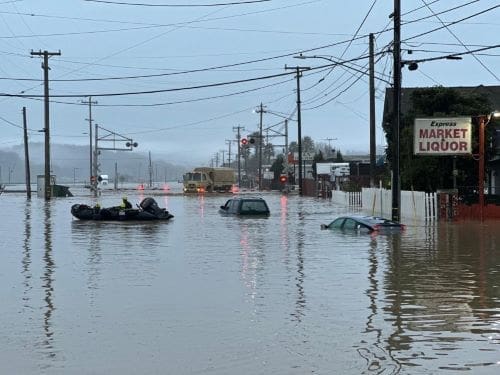 Submerged cars float in the forefront as a National Guard vehicle approaches a flooded railroad track in Monterey County California - climate change