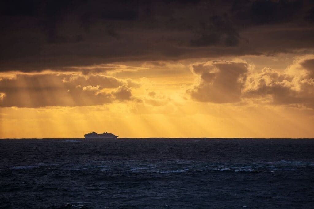 Image: Stunning shot of the calm blue ocean and the silhouette of a ship under a cloudy sky during sunset