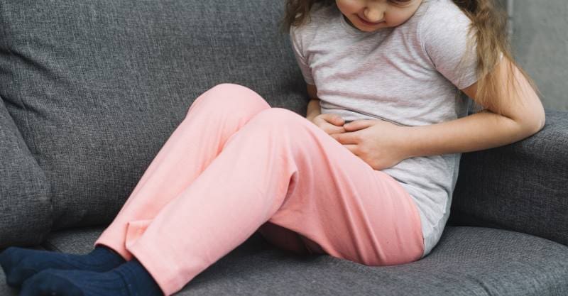 Image: Sick girl sitting on gray sofa suffers from stomach pain (s. science, climate, Muser)
