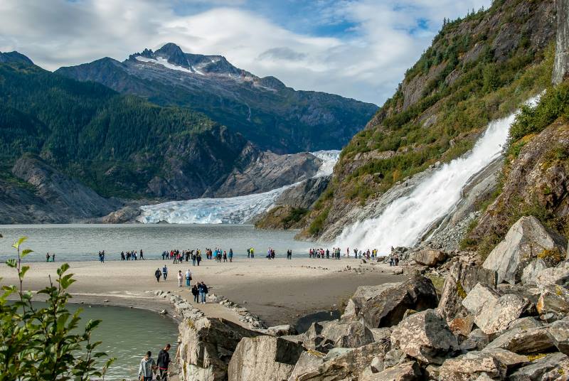 Image: people walking on beach near mountain and glacier under blue sky