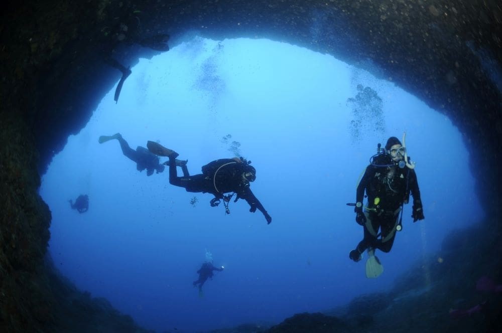 Image: a group of divers swimming in a cave
