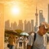 Image: Elderly man wiping sweat during a heatwave in a city street, with a large thermometer showing high temperatures and people walking under strong sunlight (s. Extreme heat)