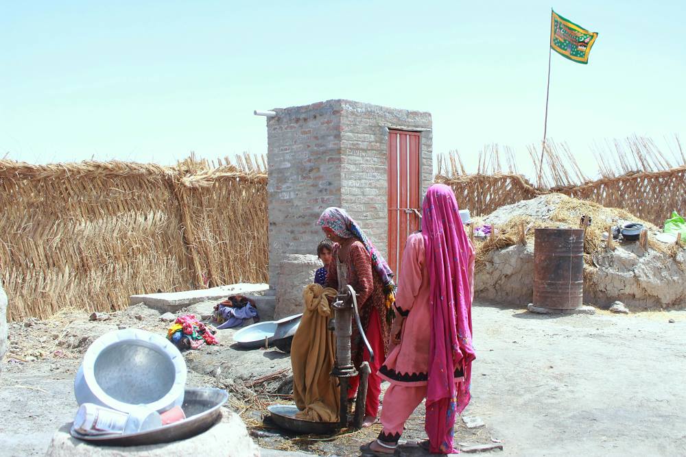 Image: Women standing outdoors in a sun-exposed rural area in Sindh, Pakistan, with dry ground and bright midday light