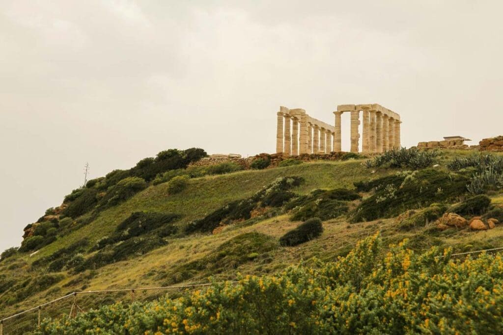 Image: large stone structure sitting on top of a lush green hillside -Sounion, Greece