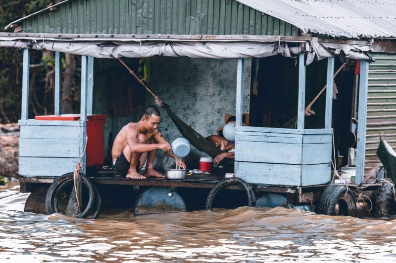 Climate change weakens social ties that save lives during disasters Image: A man sits on a flooded wooden houseboat during a heavy flood (s. climate resilience, climate change)