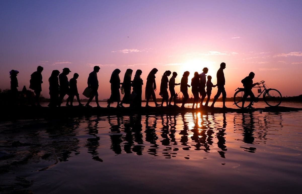 Climate change weakens social ties that save lives during disasters Image: A line of silhouetted people walking along a waterfront at sunset with reflections on the water