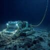 Image: Illustration of an uncrewed deep-sea mining machine operating on the seabed, connected by a cable to a surface vessel above while disturbing sediment on the ocean floor (AI-Generated)