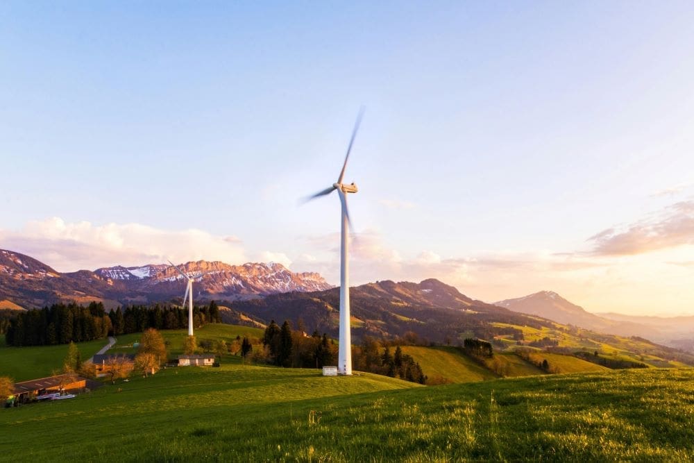 Image: A wind turbine stands tall against a mountainous backdrop under a vibrant sky at sunset